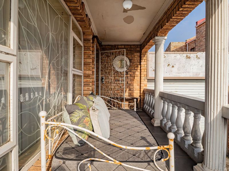 Covered balcony featuring brick walls, classic columns, and a balustrade, offering an outdoor space with potential for refurbishment.