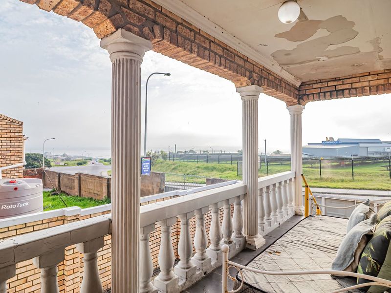 Covered balcony featuring brick columns and a balustrade, offering an elevated view of the surrounding area and street.