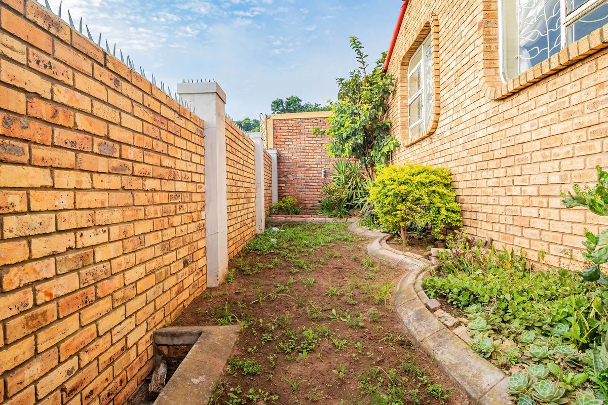A side garden area featuring face brick boundary walls with security spikes and established garden beds with concrete edging.