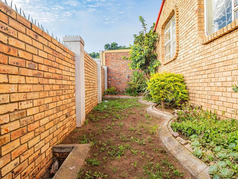 A side garden area featuring face brick boundary walls with security spikes and established garden beds with concrete edging.