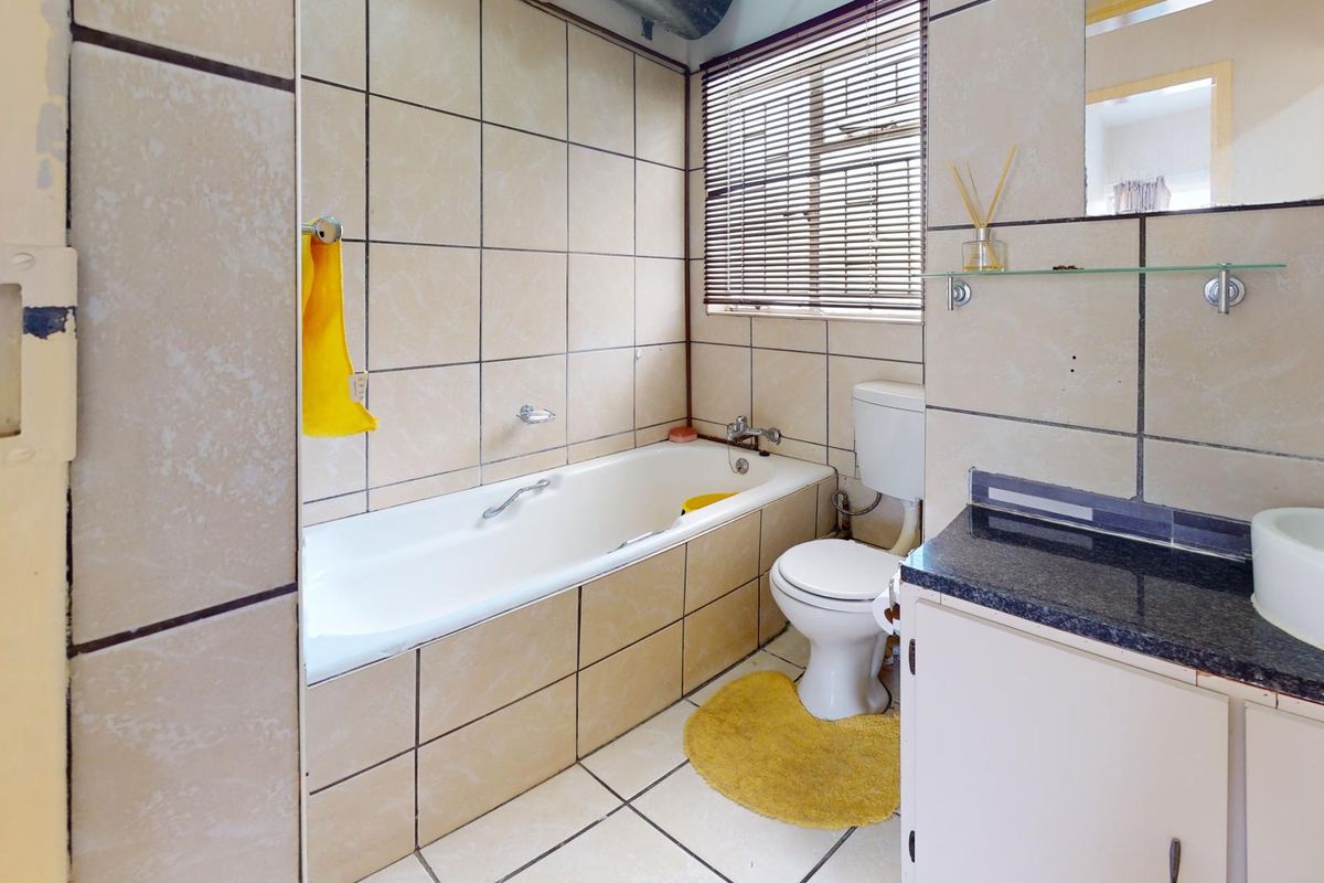 A dated bathroom featuring a built-in bathtub, toilet, and vanity with a dark countertop, finished with neutral wall and floor tiles.