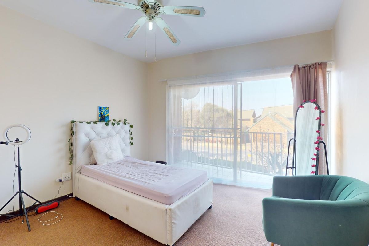 A bedroom featuring carpeted flooring, a ceiling fan, and large sliding glass doors providing access to a balcony.
