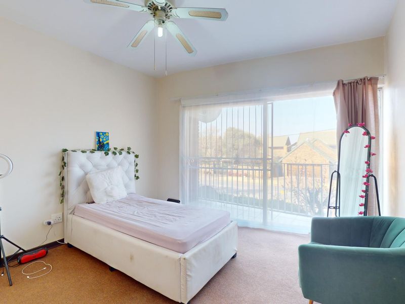 A bedroom featuring carpeted flooring, a ceiling fan, and large sliding glass doors providing access to a balcony.