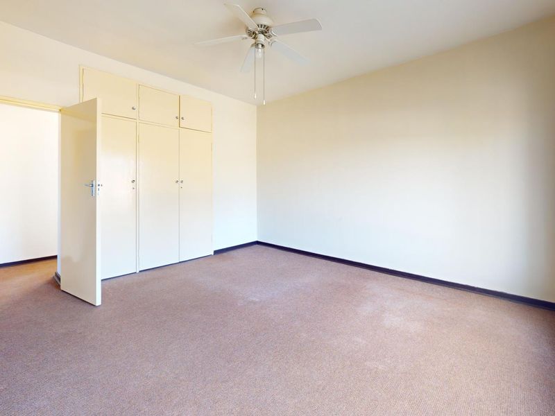 A spacious, empty bedroom featuring built-in cupboards, a ceiling fan, and large windows, providing a blank canvas for personalization.