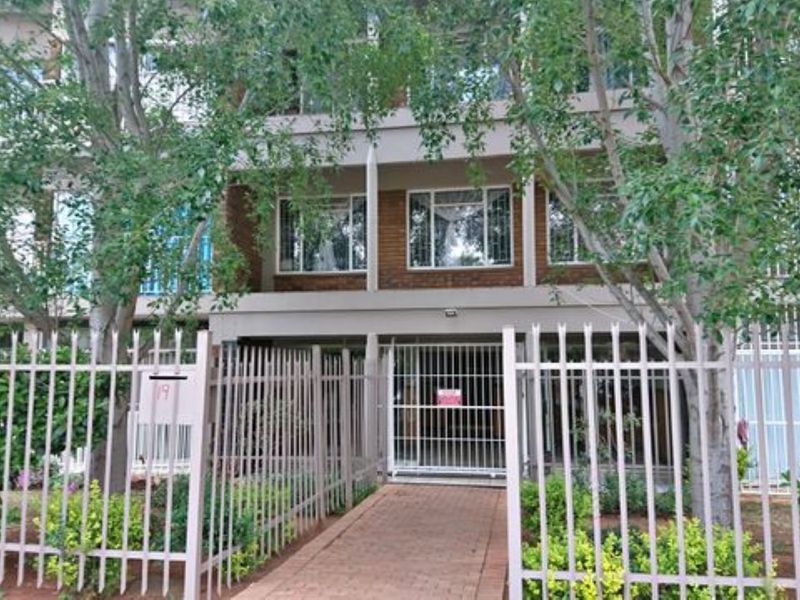 Front view of an apartment building featuring a brick facade, secure perimeter fencing, and a paved entrance walkway.