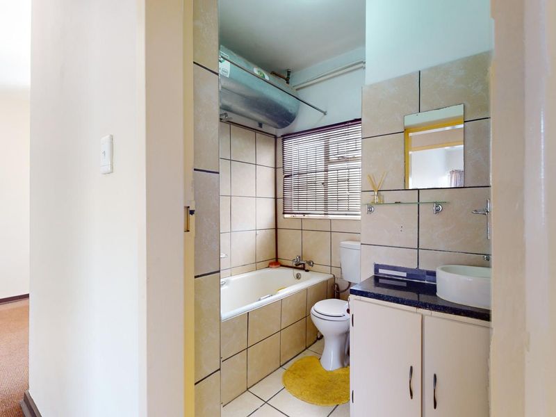 A functional bathroom featuring a built-in bathtub, vanity with basin, and tiled finishes, with an exposed water heater unit.