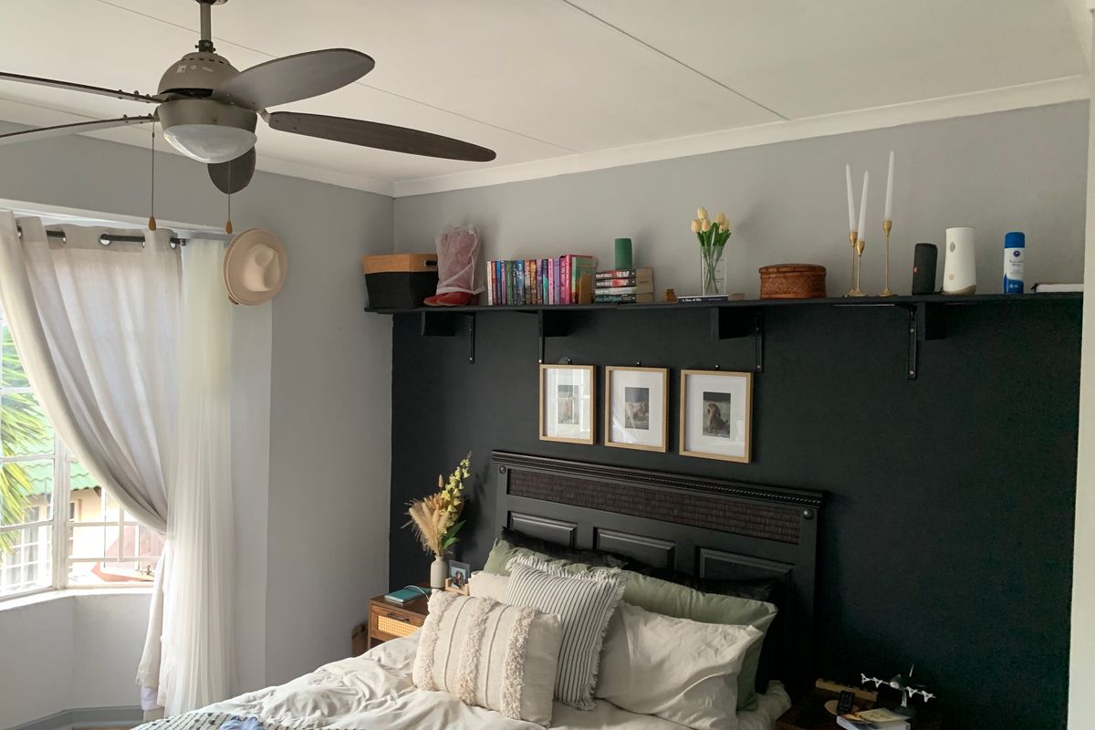 A well-maintained bedroom featuring a ceiling fan, a bay window with curtains, and a dark accent wall with built-in shelving.