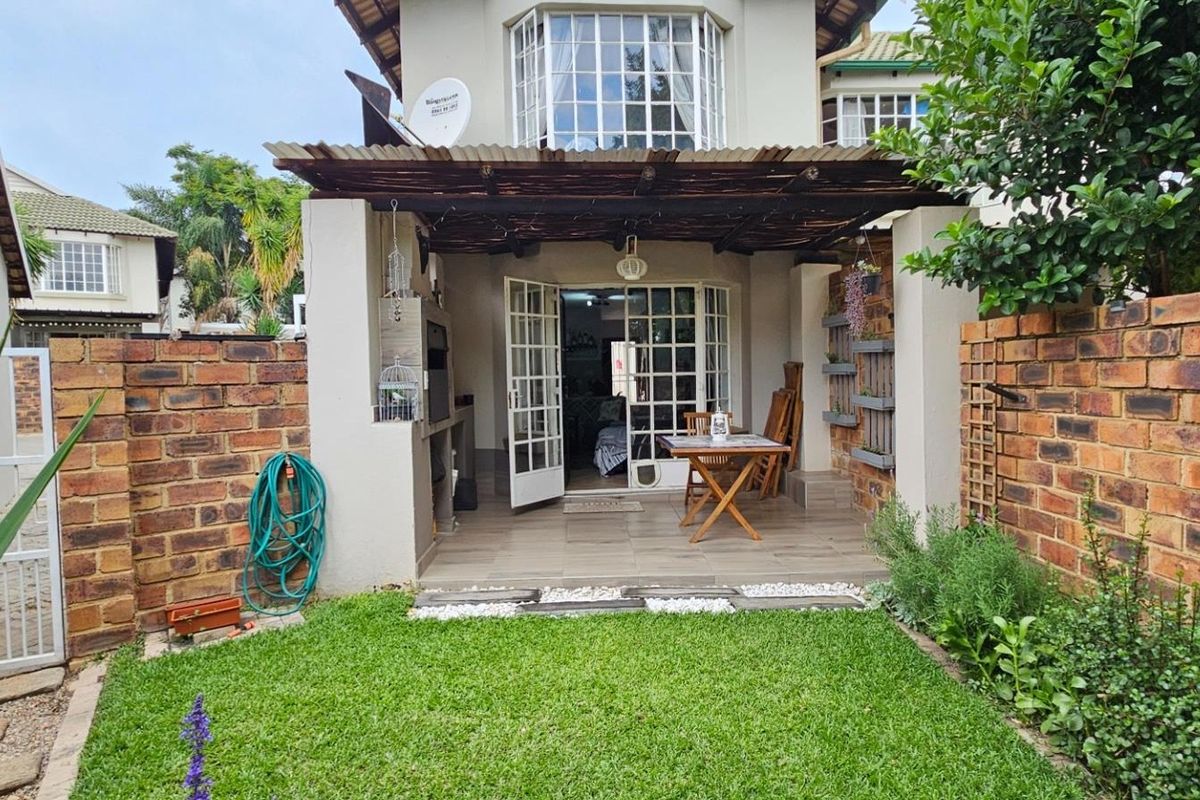 Rear exterior view of a townhouse featuring a covered patio with a built-in braai, brick boundary walls, and a small private garden.