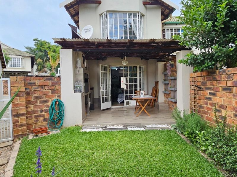 Rear exterior view of a townhouse featuring a covered patio with a built-in braai, brick boundary walls, and a small private garden.