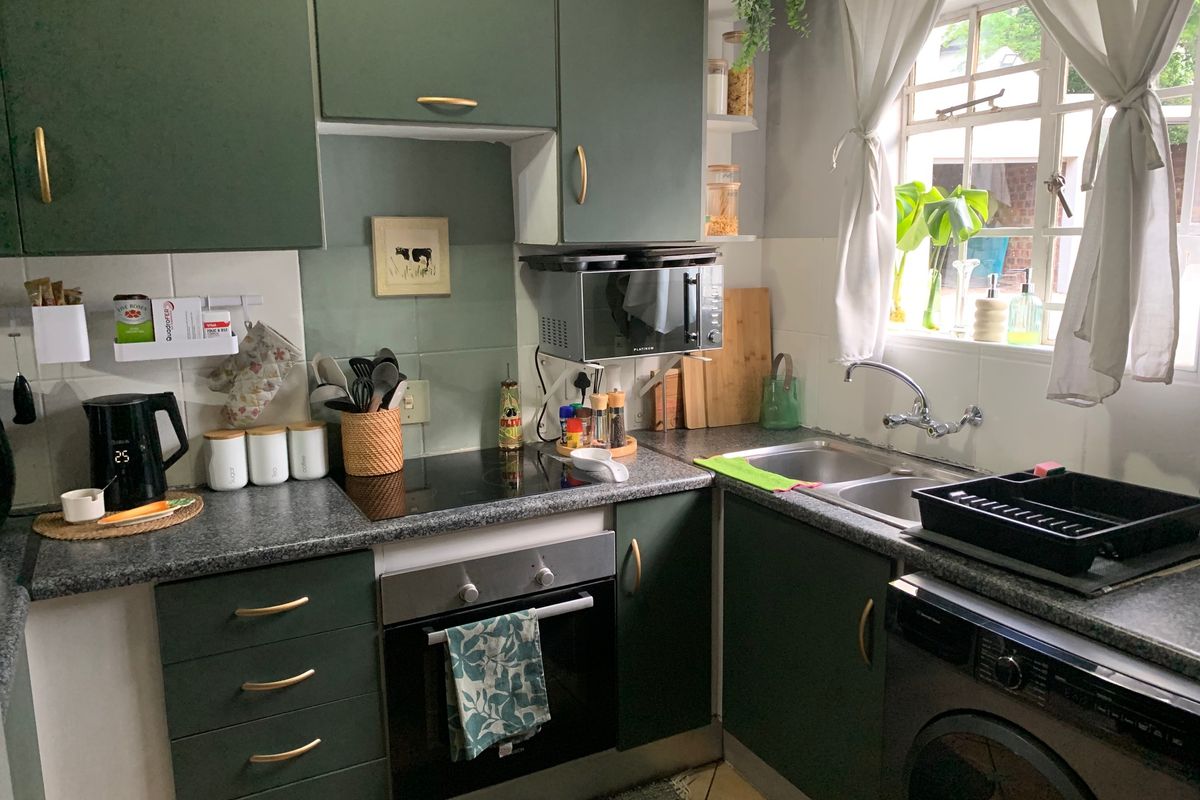 Compact kitchen featuring dark green cabinetry, laminate countertops, integrated oven and hob, and a double bowl sink with a window view.