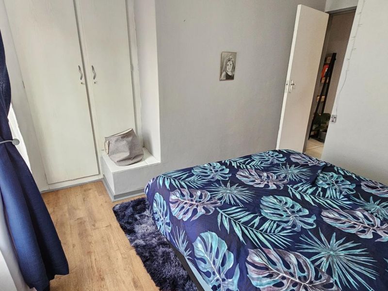 A bedroom featuring laminate flooring and a built-in wardrobe, offering a functional and neutral space for rest.