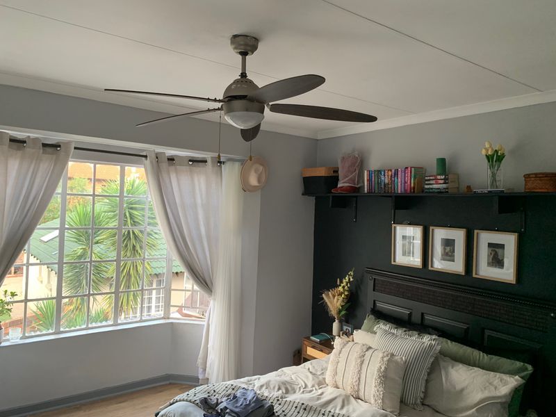 A well-lit bedroom featuring a ceiling fan, laminate flooring, and a large bay window providing natural light and exterior views.