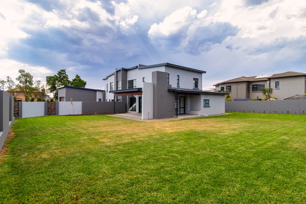 A modern two-story house exterior featuring a spacious rear garden, covered patio area, and secure boundary walls.