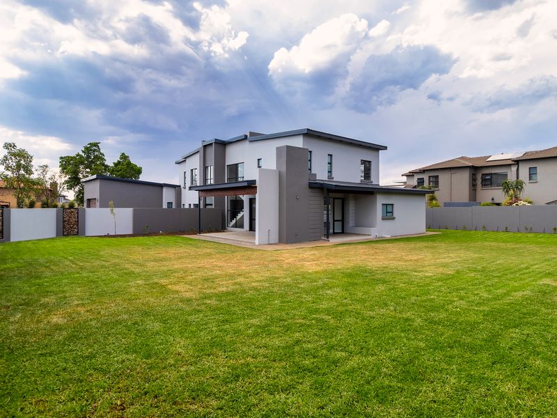 A modern two-story house exterior featuring a spacious rear garden, covered patio area, and secure boundary walls.