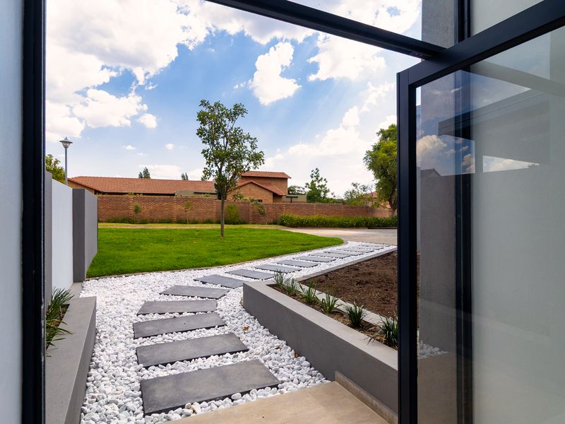 A well-maintained rear garden featuring a modern stone paver walkway, white gravel landscaping, and a neat lawn enclosed by a brick boundary wall.