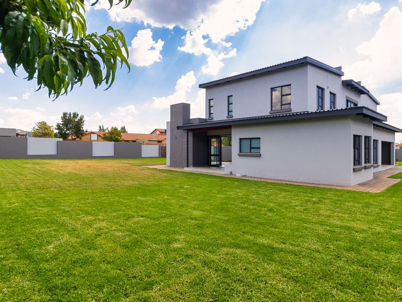 Rear view of a modern double-storey house featuring a large manicured lawn, paved patio area, and secure boundary walling.