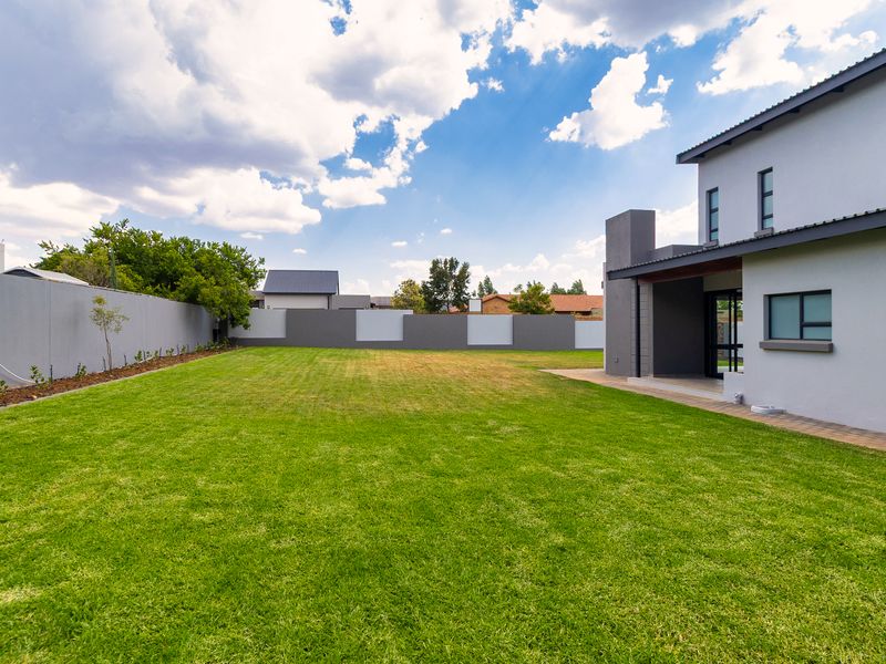 Spacious rear garden featuring a well-maintained lawn, perimeter boundary walls, and a paved patio area adjacent to the modern house structure.