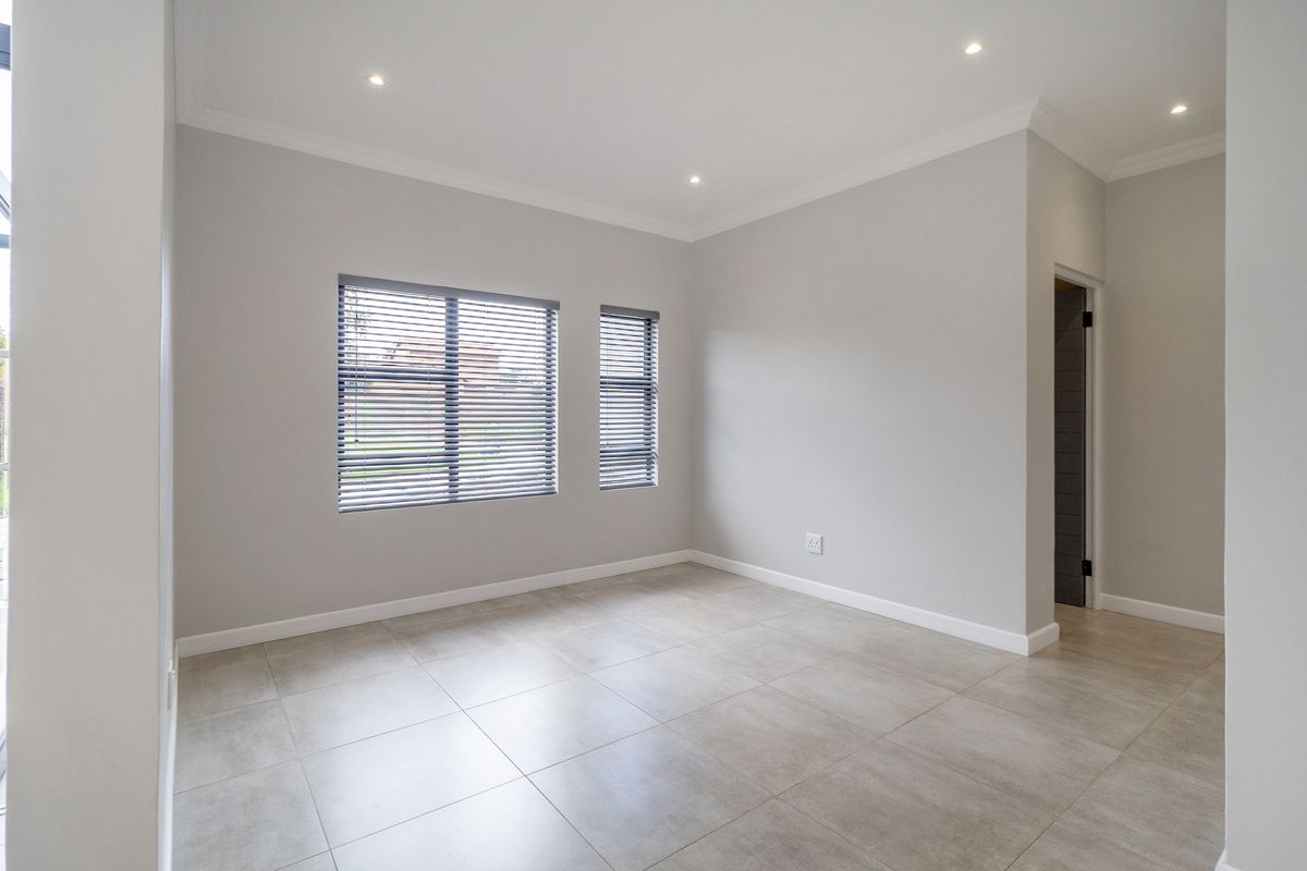 A bright, empty bedroom featuring neutral grey walls, large tiled flooring, recessed downlighting, and modern venetian blinds.