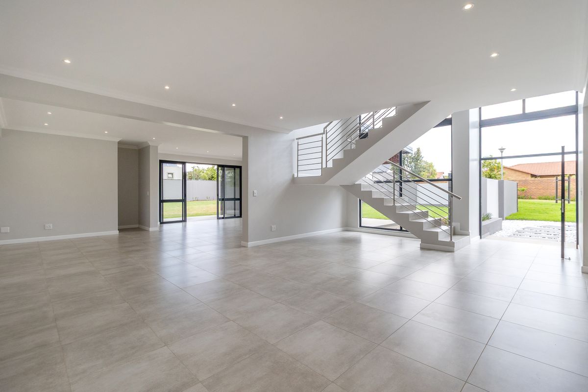 Spacious, modern open-plan living area featuring large format floor tiles, a contemporary staircase with stainless steel balustrades, and expansive glass doors leading to the garden.