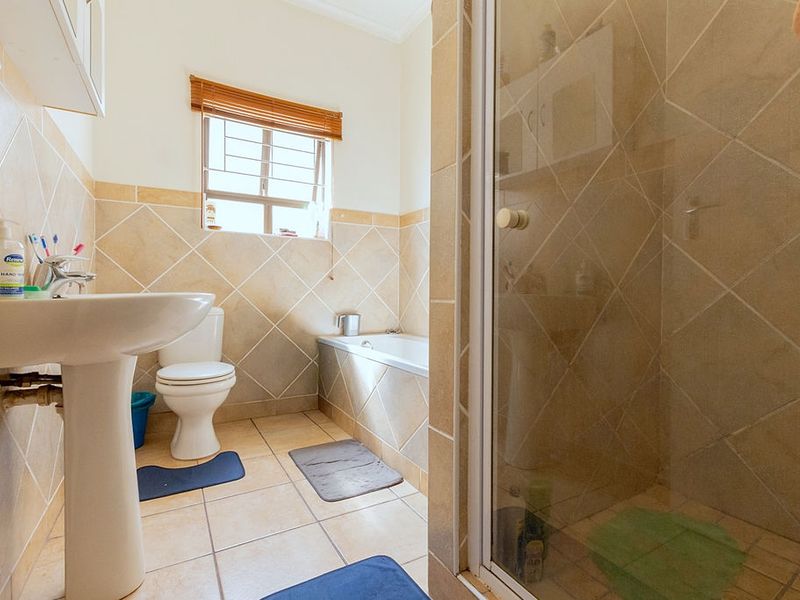 A functional bathroom featuring a pedestal basin, toilet, bathtub, and a separate shower enclosure with neutral tiled finishes.