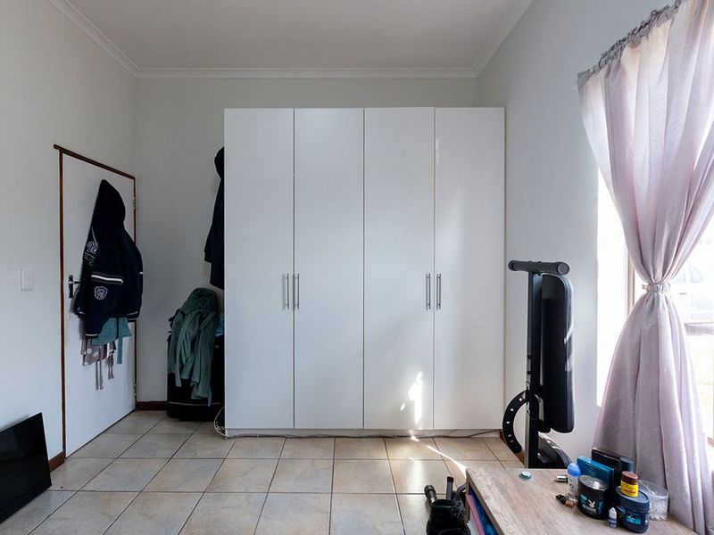 A bedroom featuring tiled flooring and a large white built-in wardrobe with modern handles.