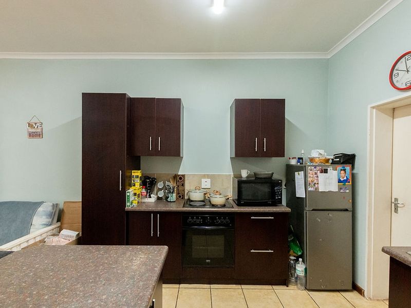 A functional kitchen featuring dark wood cabinetry, laminate countertops, a built-in oven, and a hob, set against light-colored walls with tiled flooring.