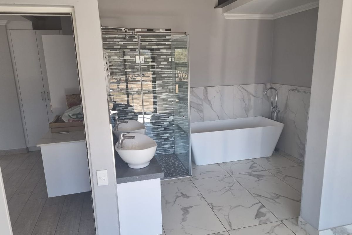 Modern bathroom featuring a freestanding bathtub, glass-enclosed shower, dual vessel sinks on a vanity, and elegant marble-look floor tiling.