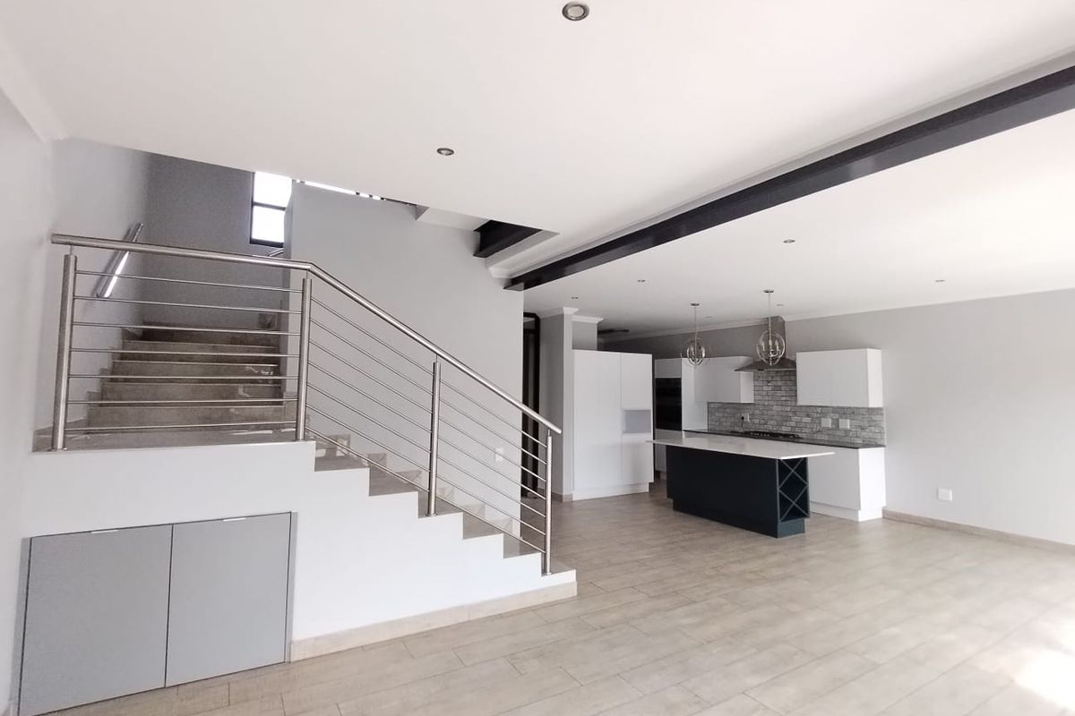Spacious open-plan living area featuring a modern kitchen with island, stone backsplash, and a striking staircase with stainless steel railing.