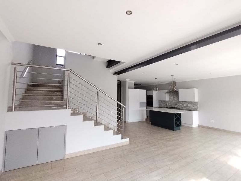 Spacious open-plan living area featuring a modern kitchen with island, stone backsplash, and a striking staircase with stainless steel railing.