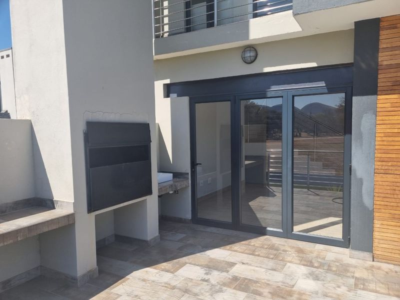 Covered patio area featuring a built-in braai with stone counter, tiled flooring, and modern folding glass doors leading into the home.