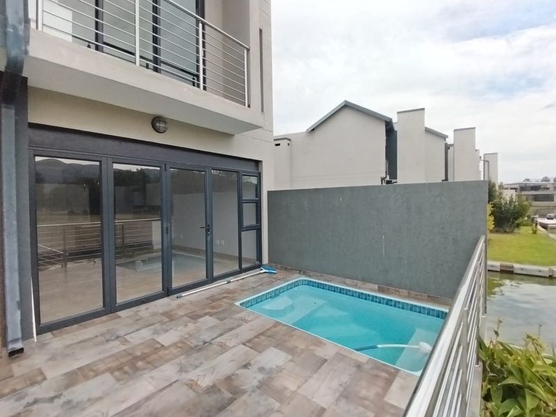 A modern patio area featuring a private plunge pool, tiled flooring, and large aluminium stacker doors leading into the residence.