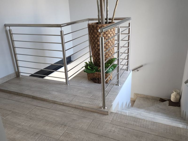 A bright hallway featuring a modern stainless steel balustrade and contemporary wood-look tile flooring leading down a staircase.
