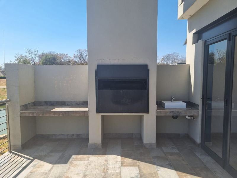 Covered patio area featuring a built-in braai, stone prep counters, and a small basin, ideal for outdoor entertaining.