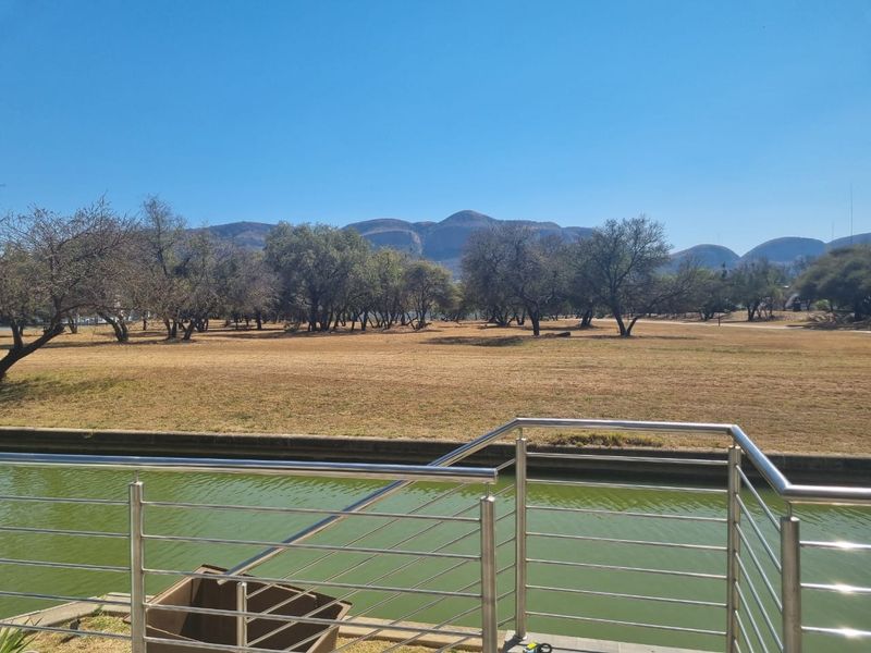 Scenic view overlooking a canal and expansive open landscape with mountain vistas in the background, featuring a modern stainless steel balustrade.