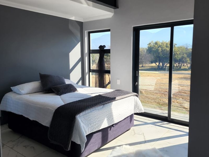 Modern bedroom featuring large format floor tiles, an exposed steel beam, and sliding glass doors providing scenic views and natural light.