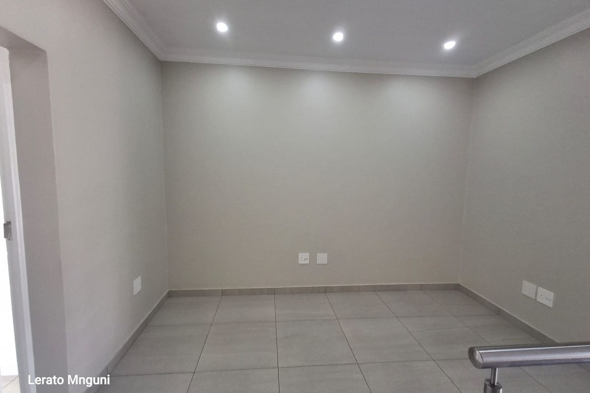 A clean, empty living space featuring neutral wall tones, modern ceramic floor tiles, recessed downlighting, and a contemporary stainless steel balustrade.