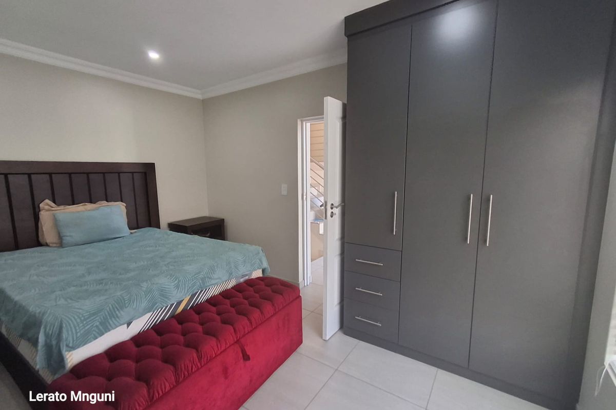 A well-maintained bedroom featuring modern dark grey built-in cupboards, neutral tiled flooring, and recessed ceiling lighting.