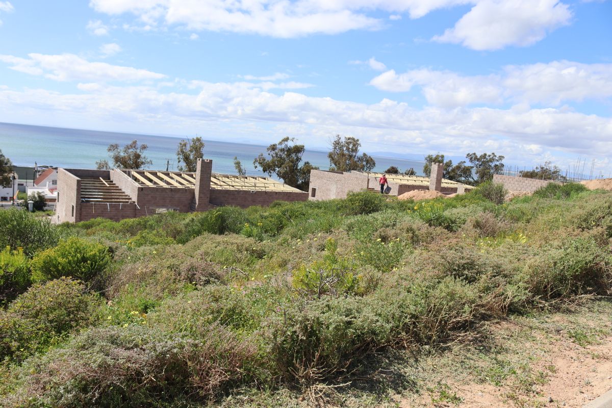 A view of a residential property under construction, featuring masonry walls and timber roof trusses, set against a coastal landscape.