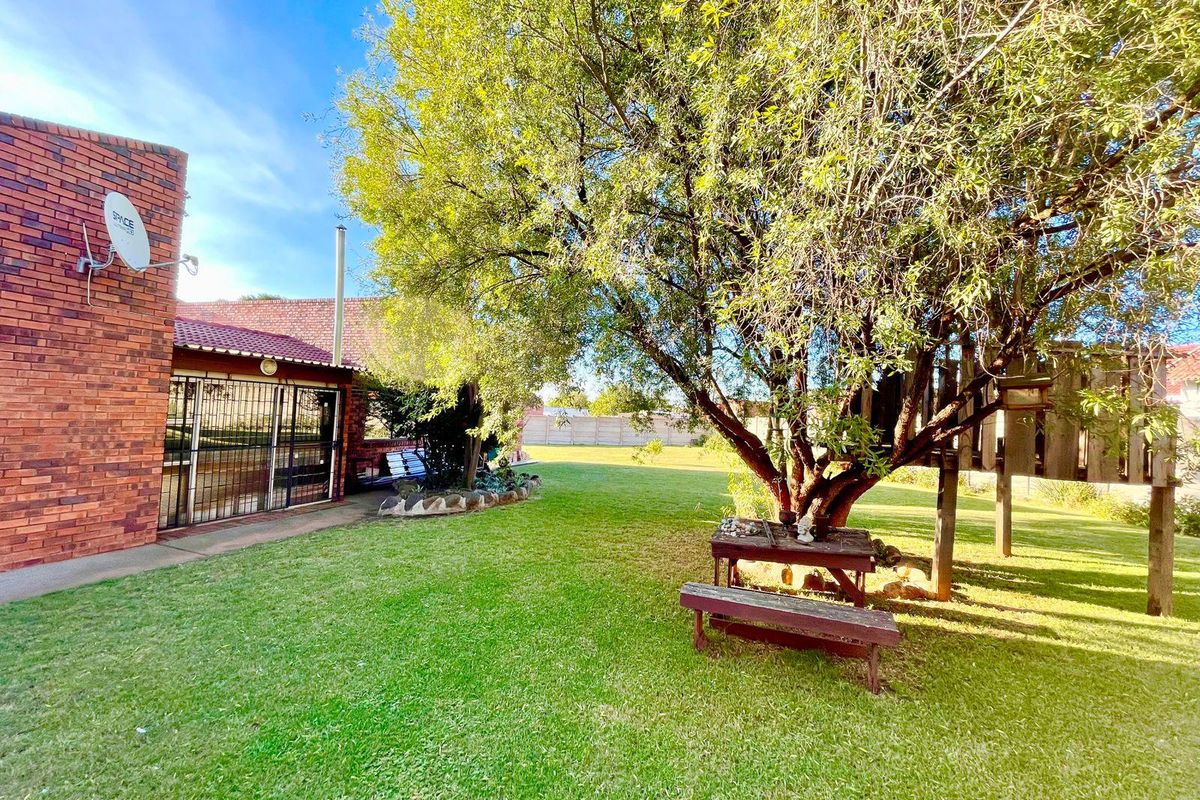 A spacious rear garden featuring a well-maintained lawn, mature trees, and a brick-built exterior facade with security gates.