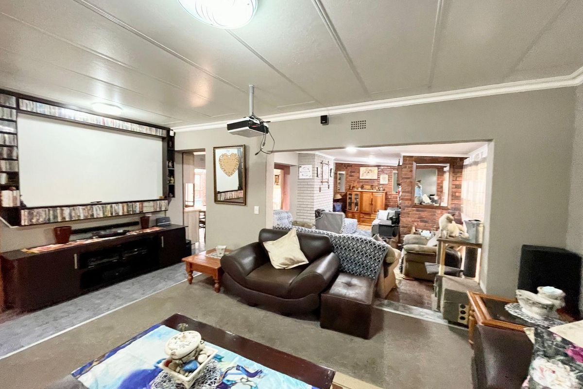 Spacious living area featuring a built-in media wall with projector setup, opening into an adjacent room with exposed brick accents.