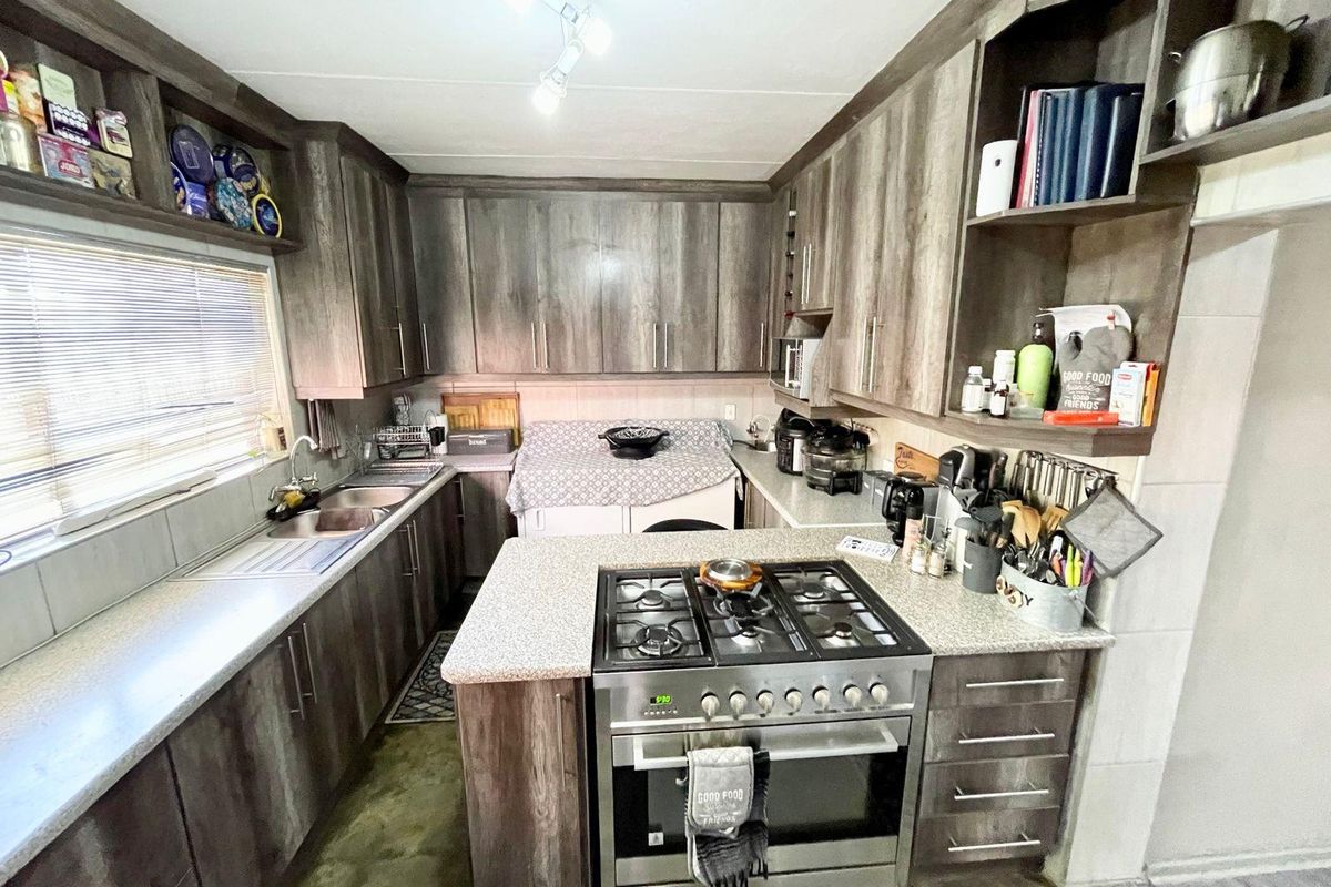 A functional kitchen featuring wood-grain cabinetry, granite-look countertops, a built-in gas hob and oven, and a double stainless steel sink.