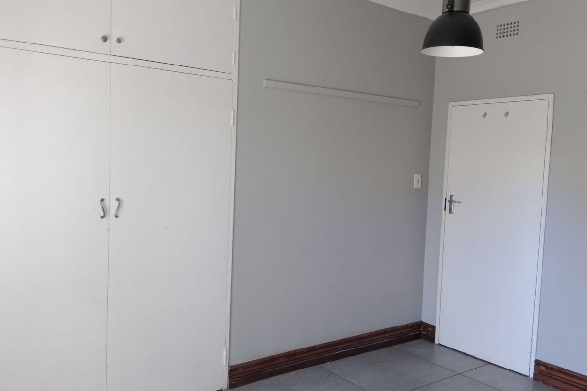 A clean, empty bedroom featuring neutral grey walls, tiled flooring, and built-in storage cupboards.