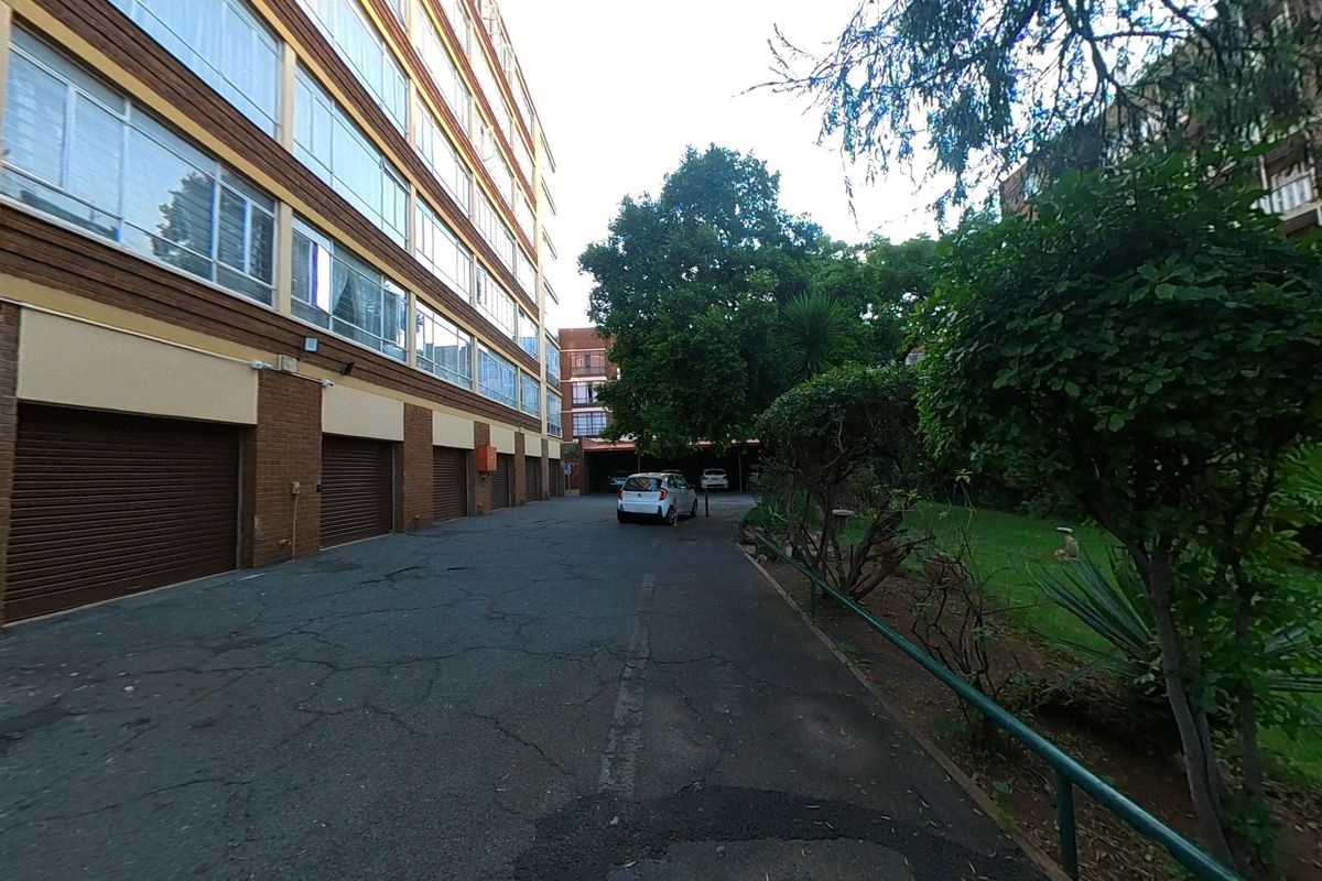 Rear exterior view of the apartment complex featuring a paved driveway, multiple roller garage doors, and an adjacent landscaped garden area.