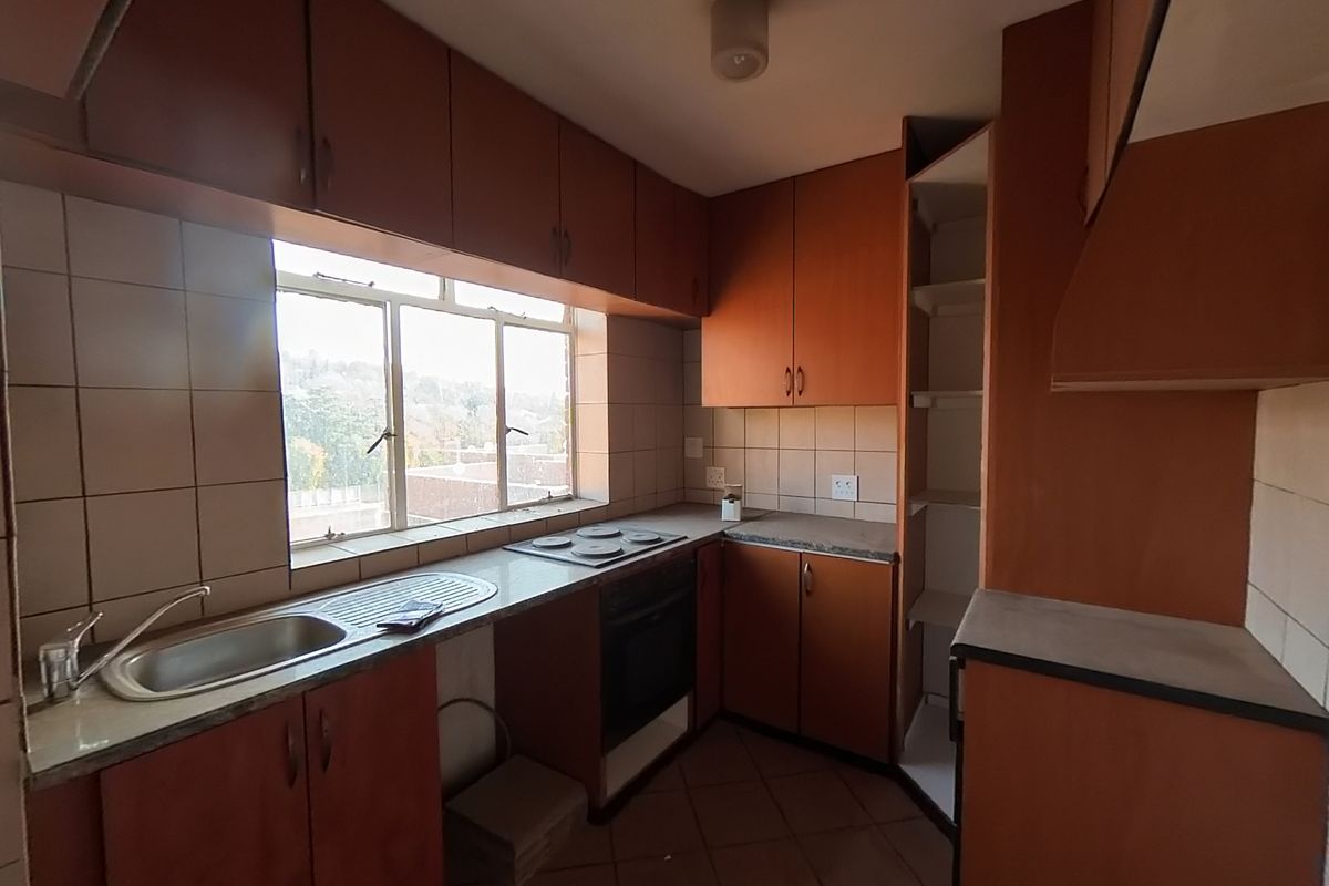 A dated kitchen featuring built-in wooden cabinetry, laminate countertops, an integrated electric hob and oven, and tiled splashbacks.