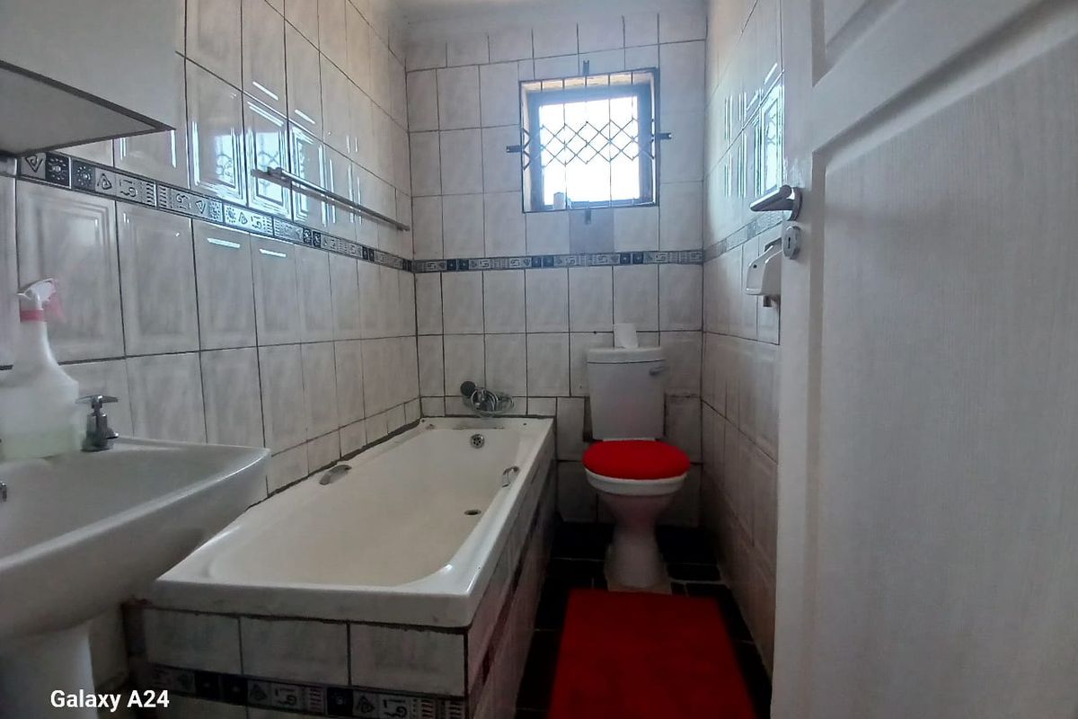 A compact bathroom featuring a bathtub, pedestal basin, and toilet with dated wall tiling and a security-fitted window.