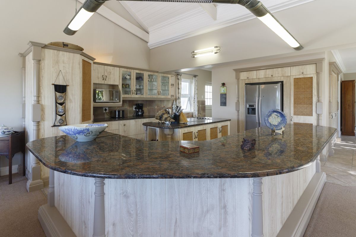 Spacious kitchen featuring a large granite-topped island, custom cabinetry, vaulted ceilings, and integrated appliances, offering a functional and well-maintained culinary space.