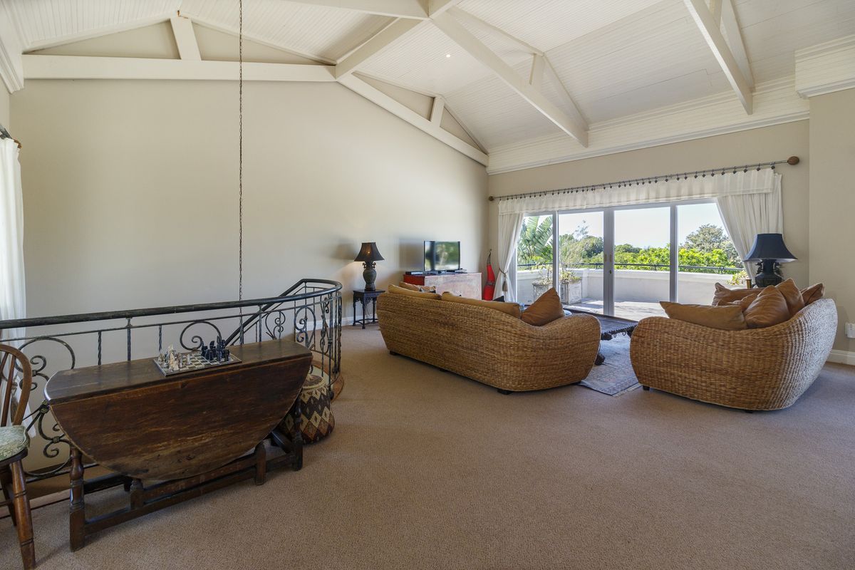 Spacious living room featuring a high vaulted ceiling with exposed rafters, carpeted flooring, and large sliding glass doors leading to an outdoor balcony.