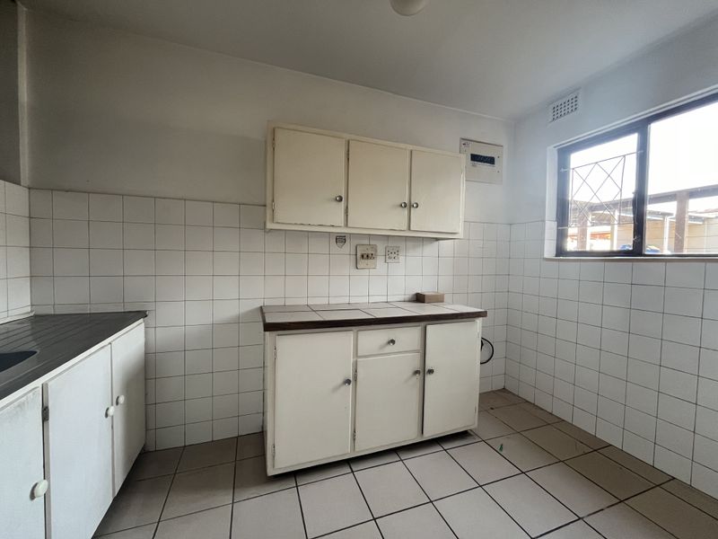 A functional, empty kitchen space featuring tiled flooring, white wall tiles, and built-in cabinetry, offering a blank canvas for modern renovation.