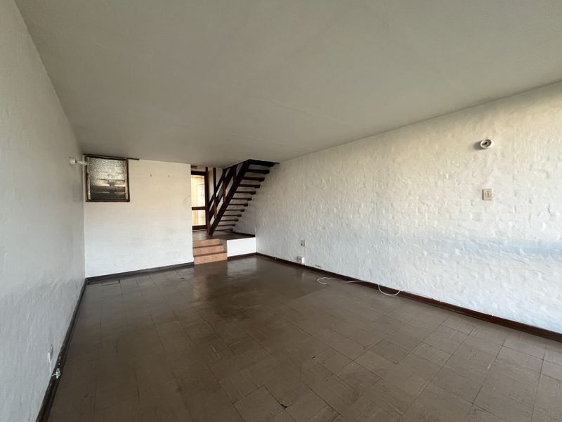 An empty living room featuring textured walls, tiled flooring, and an internal staircase leading to an upper level.