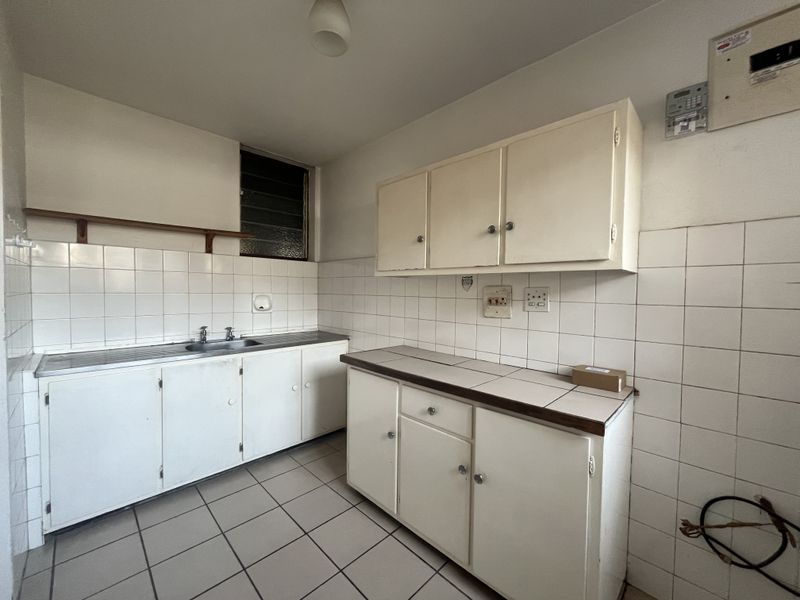 A dated, empty kitchen featuring original built-in cabinetry, tiled splashbacks, and tiled flooring, offering a blank canvas for modern renovation.